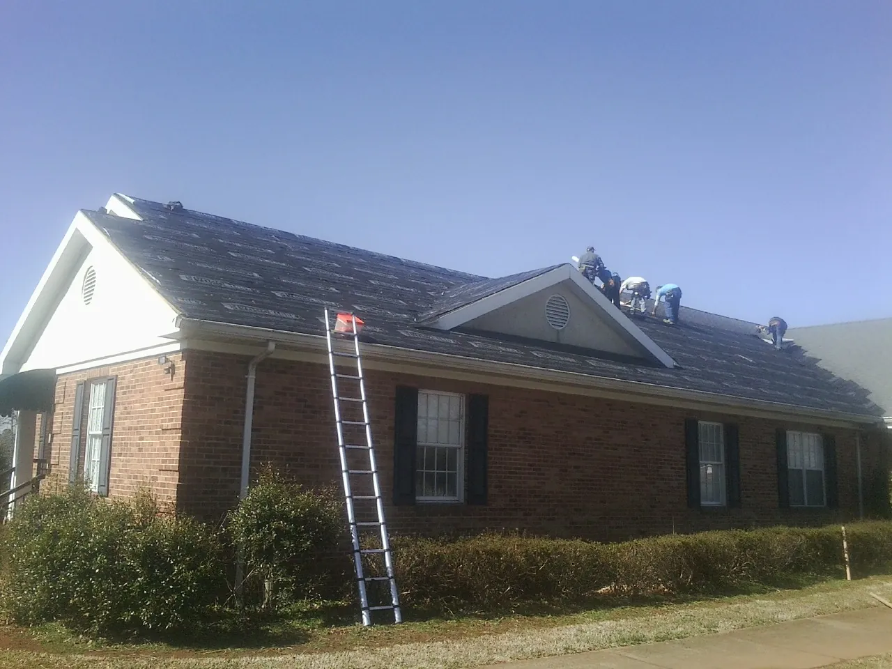 Crew tearing shingles off a brick ranch roof with a ladder set — Metal Roof Repair work by our crew in Elberfeld