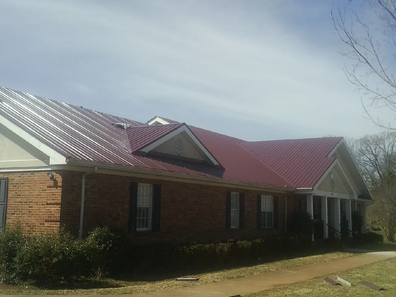 Red metal roof with gabled entries on a long brick building, from a Hail Damage Roof Repair job in Elberfeld