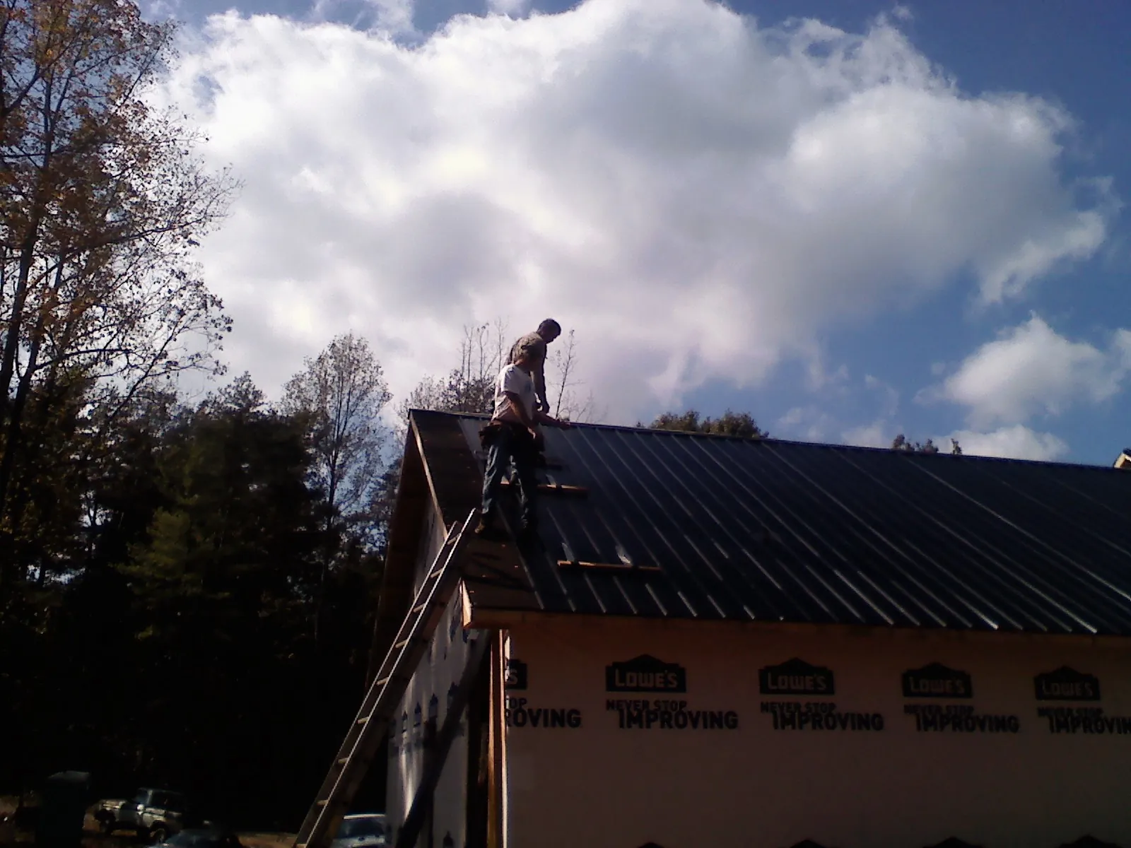 Roofer fastening dark metal panels high against a cloudy sky, from a Roof Inspection job in Elberfeld