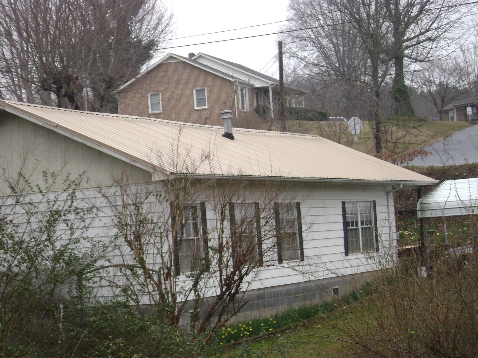 Tan metal roof on a white sided house set into a hillside — Commercial Roofing by Roofing Brothers in Elberfeld