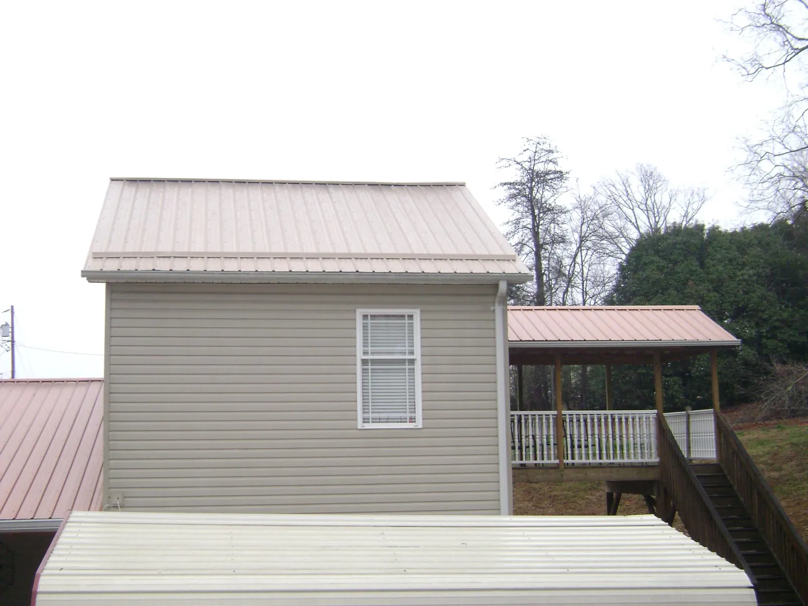 Tan metal roofs on a two story addition and attached porch, from a Roof Replacement job in Elberfeld